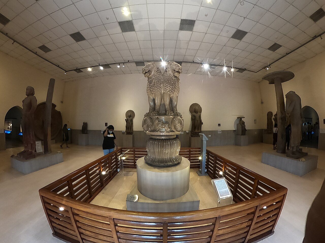 Photograph of the Lion Capital of Ashoka, four sandstone lions back to back on a drum carved with wheels, displayed in the Sarnath museum