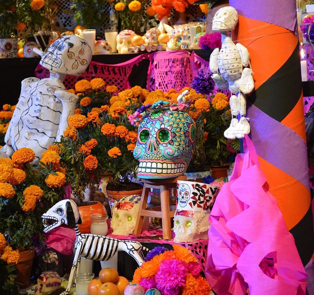 Photo of a Day of the Dead ofrenda piled with orange marigolds, painted skulls, candles, oranges and papier-mâché skeletons