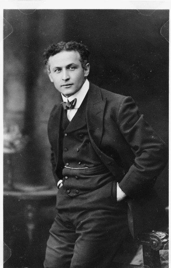 Studio photograph of Harry Houdini in a three-piece suit and bow tie, leaning on a chair, about 1913