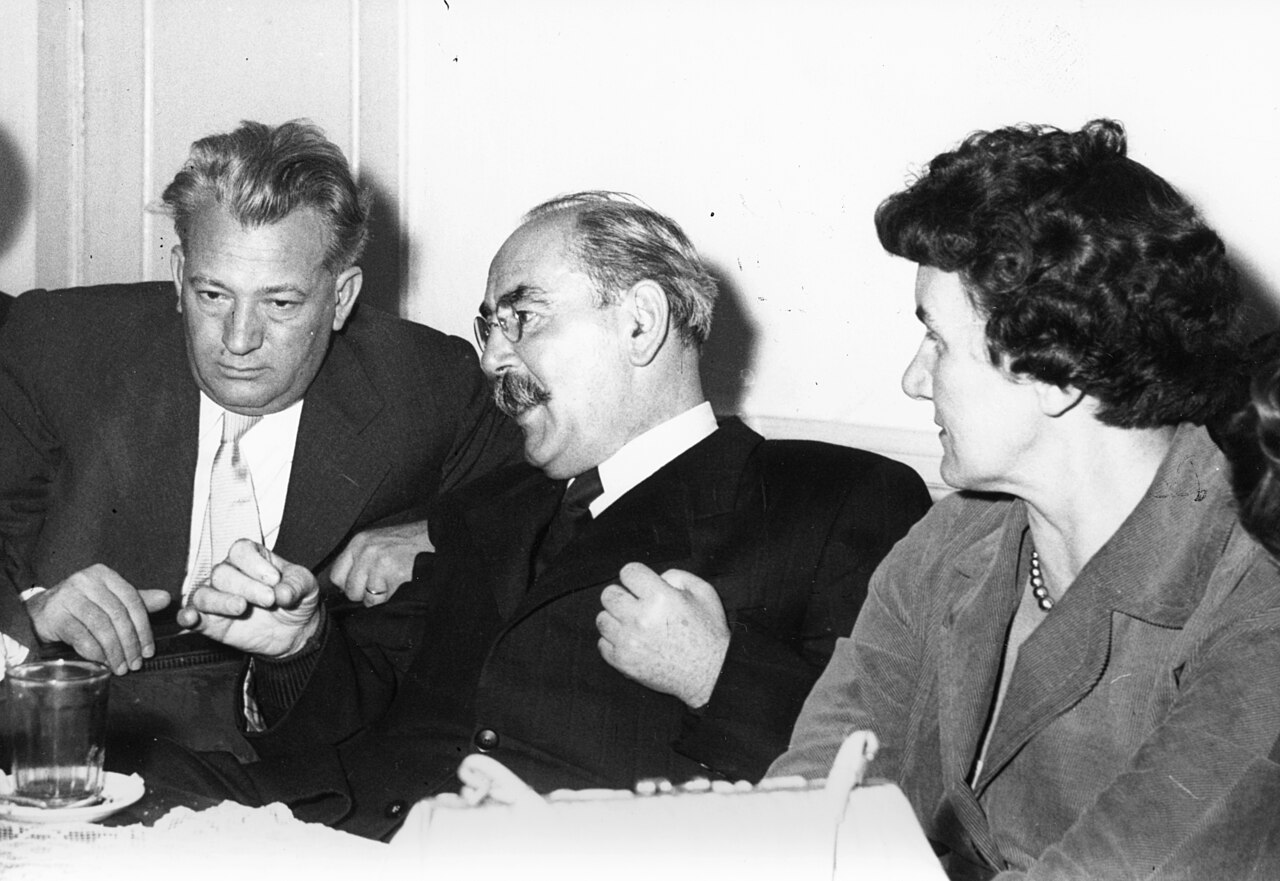 Imre Nagy, in glasses and a dark suit, seated at a table between József Darvas and Júlia Rajk at a reunion in the Kossuth Club, Budapest, 13 October 1956