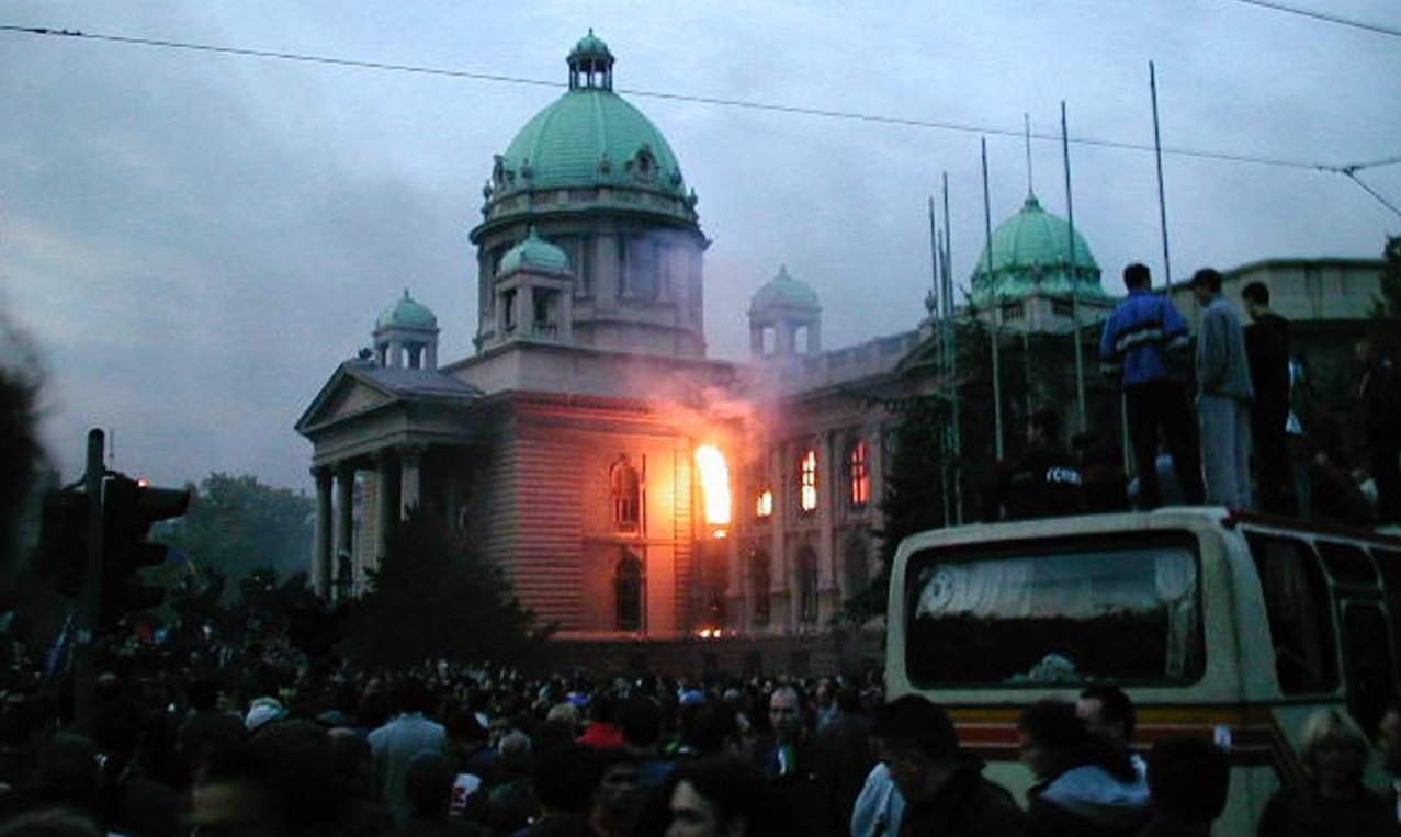 Photograph of the Yugoslav federal parliament building in Belgrade with flames in its windows and a crowd in front of it on 5 October 2000