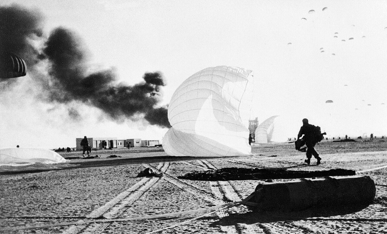 Photograph of British paratroopers landing at Gamil airfield near Port Said in November 1956, with smoke rising behind them