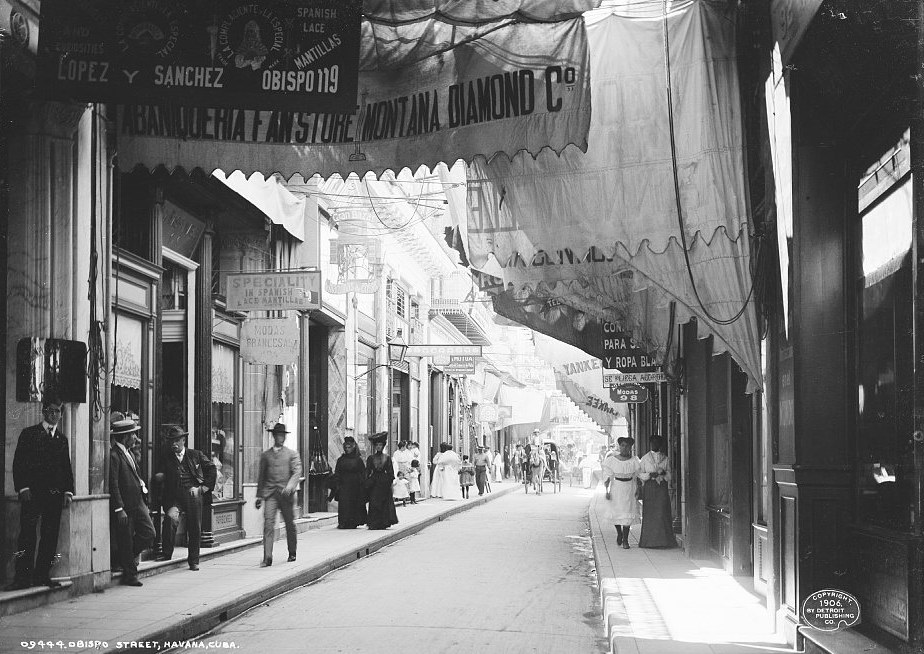 Photograph of Obispo Street in Havana around 1906, with shop awnings, signs in Spanish and English and people on the pavements