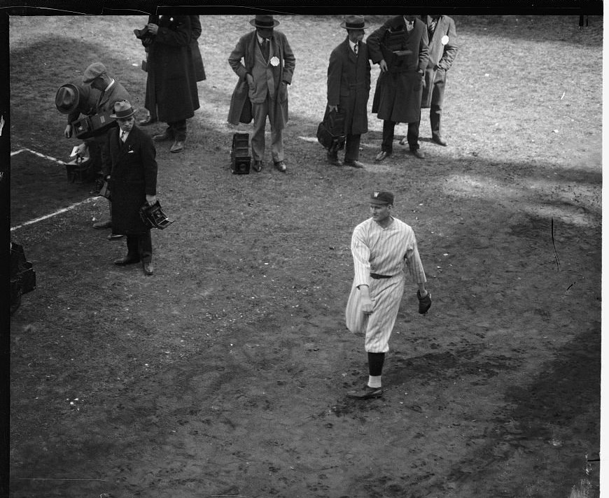 Black-and-white photograph of Washington pitcher Walter Johnson walking across the infield past a row of press photographers during the 1925 World Series